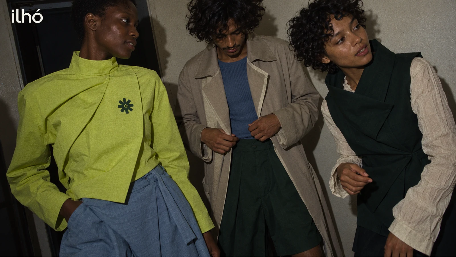 Ilhó backstage trio in sculptural lime, stone and ink-green garments, with the original white wordmark at the upper left